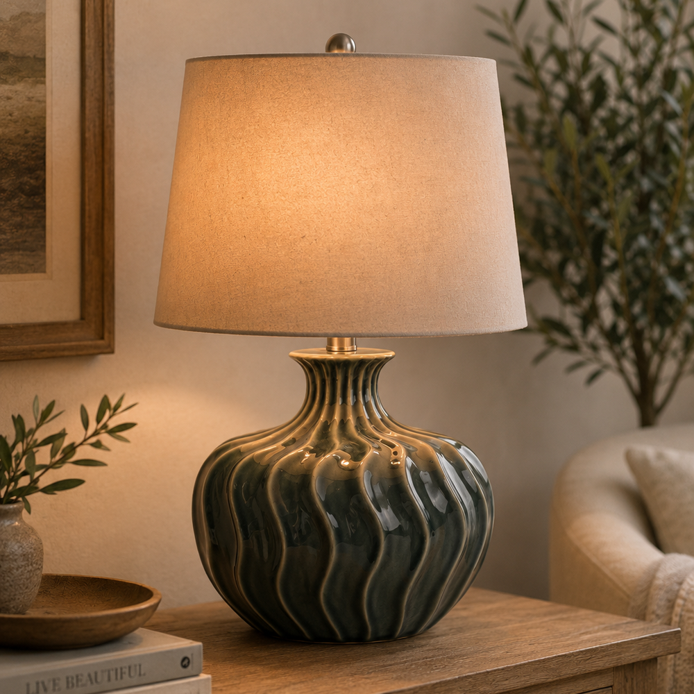 Decorative table lamp with wavy design on a wooden surface, surrounded by books and a plant.