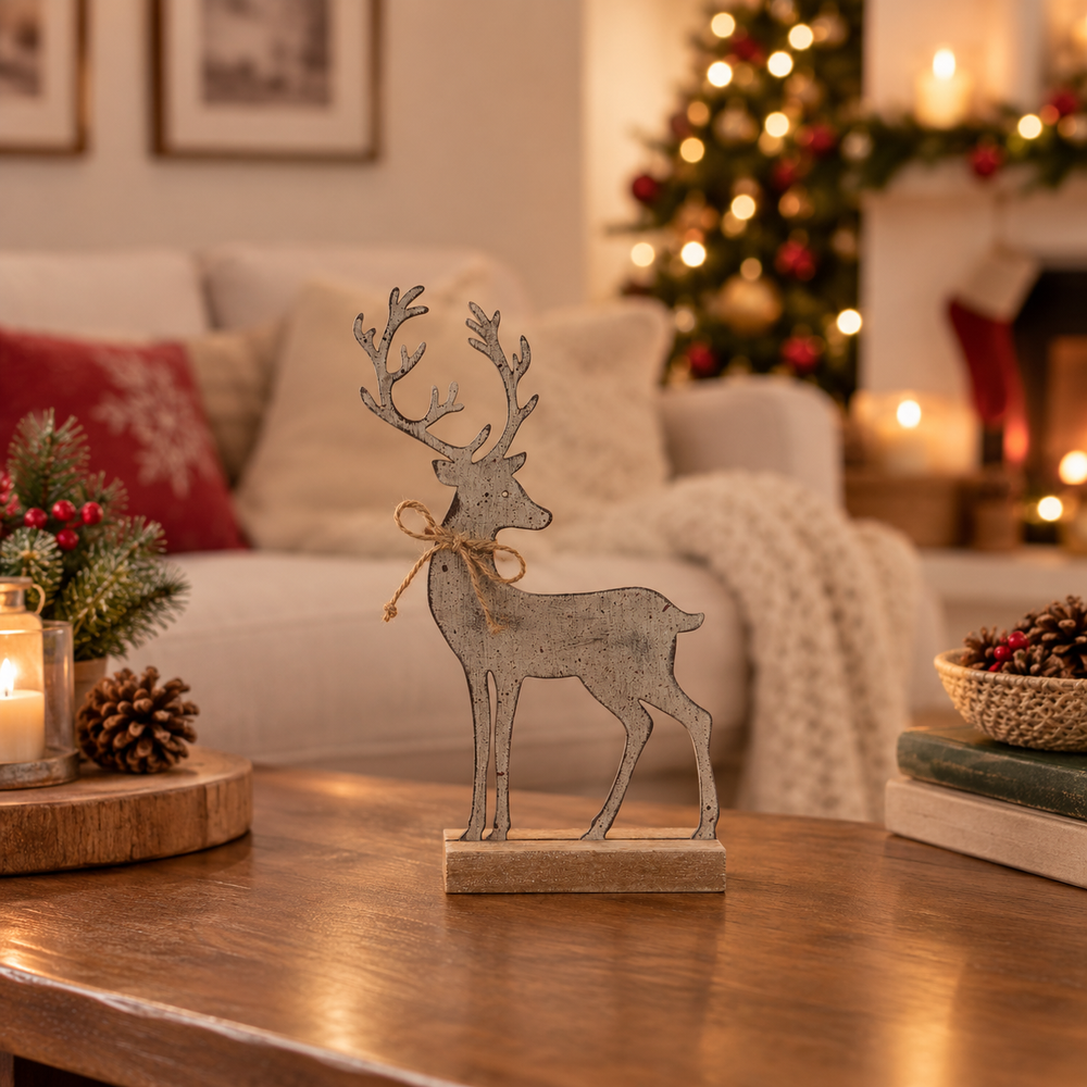 A rustic metal reindeer figurine with antlers and a twine bow stands on a wooden base on a coffee table in a cozy, warmly lit living room with a Christmas tree in the background.