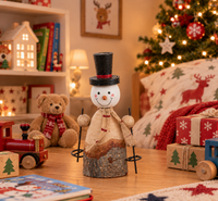 A decorative snowman figurine stands on a wooden surface in a cozy holiday room setting, with a teddy bear, toy train, wrapped gifts, and a Christmas tree in the background.